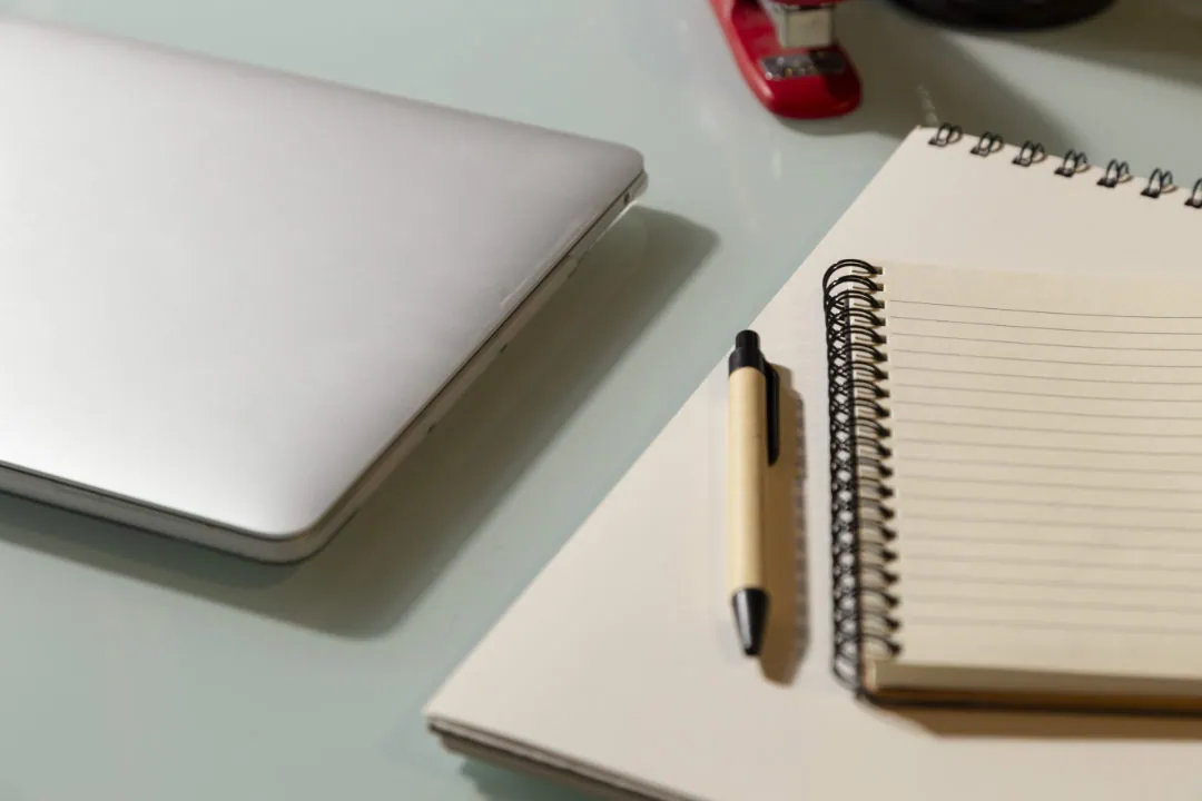 A notebook and pen near a laptop