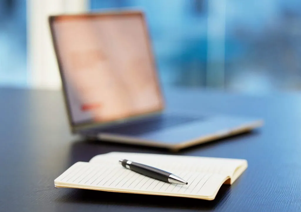 A notebook and pen near a laptop